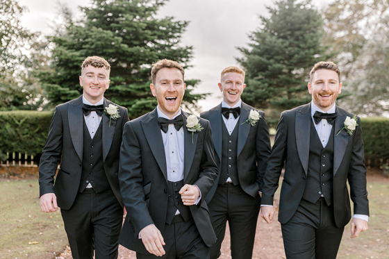 Groom and groomsmen in black tie suits walking outdoors on the wedding morning