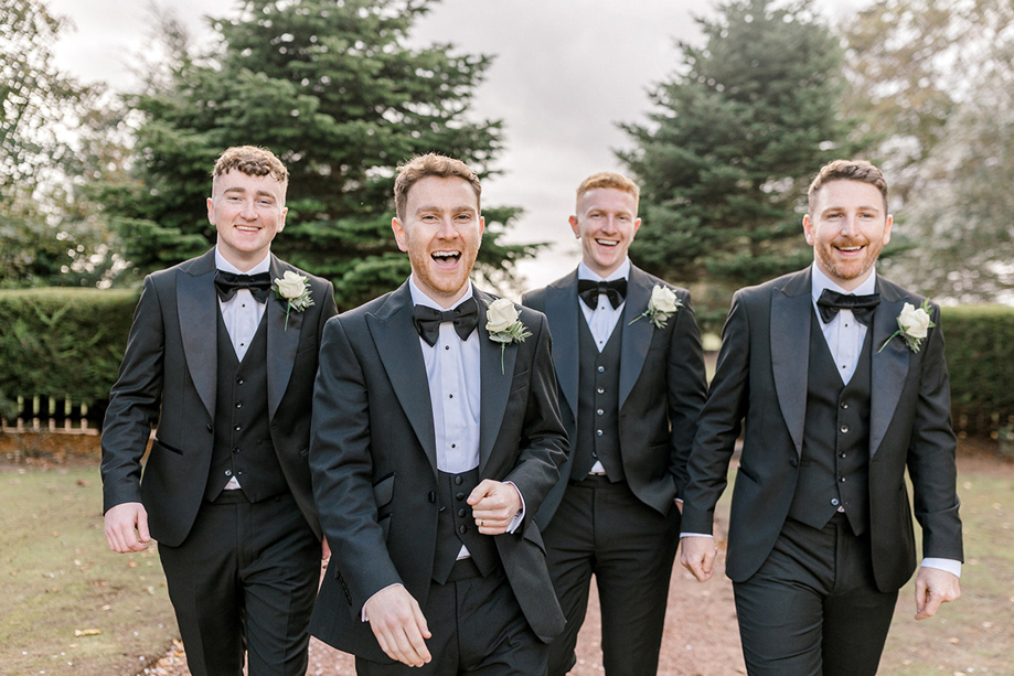 Groom and groomsmen in black tie suits walking outdoors on the wedding morning