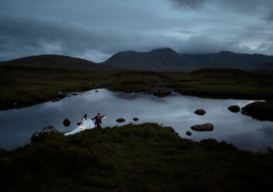 Eloping couple walking through the moors holding lanterns in Glencoe, Scotland