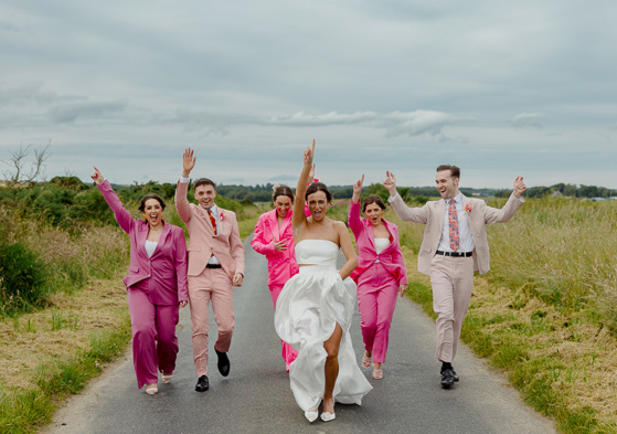 A bride and her bridal party dance down a country road