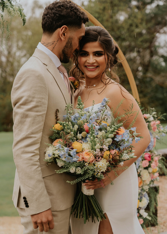 Bride holding spring pastel bouquet and standing with groom