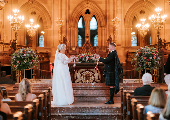 Bride and groom doing handfast at altar with floral arrangements around them