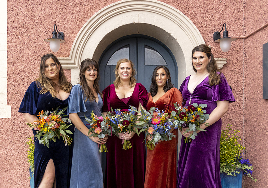 Bridesmaids in colorful velour dresses hold colourful bouquets