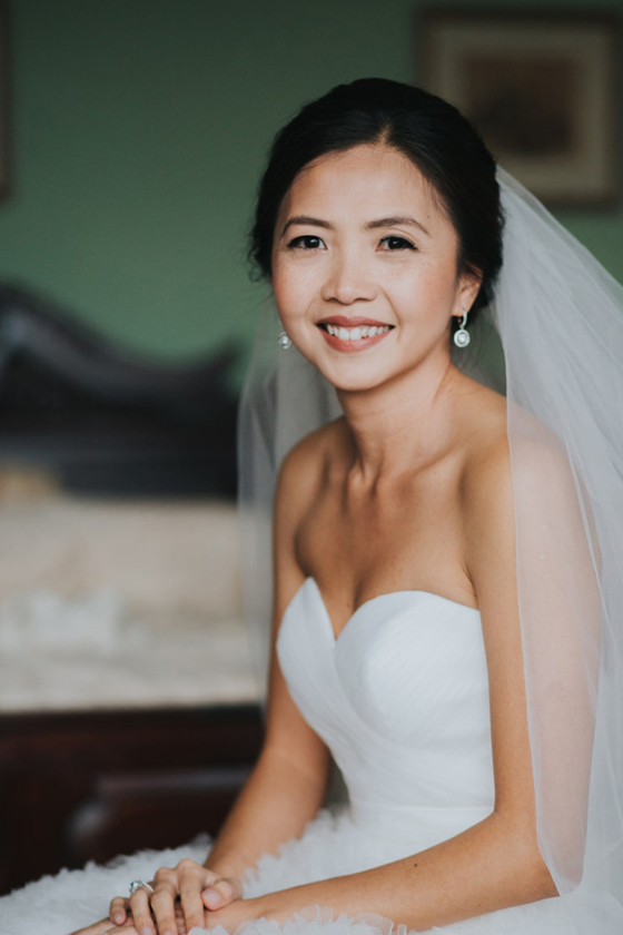 Bride smiles in hotel room before her wedding, makeup is by Jennifer Louise Studio.