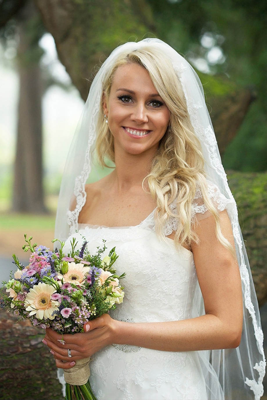 Bride holds a small colourful bouquet and poses outside, makeup by Jennifer Louise Studio.
