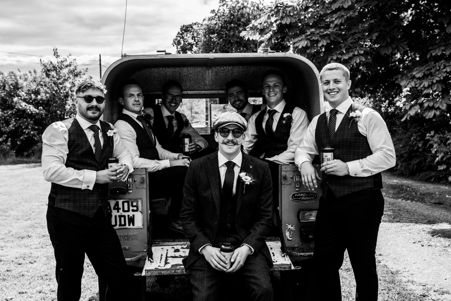 Groomsmen pose at boot of old car.