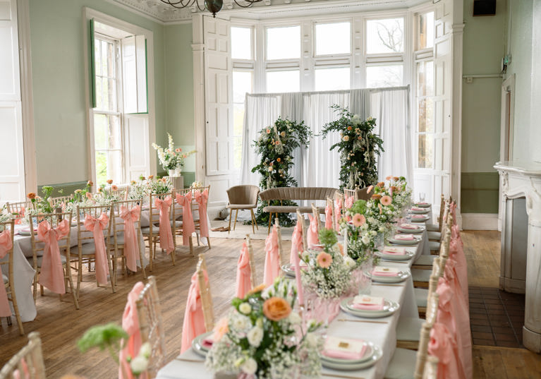 Image of wedding meal set up with pink chair ribbons and floral centrepieces