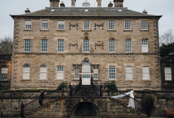 Bride walking down stairs outside venue with veil blowing in wind behind