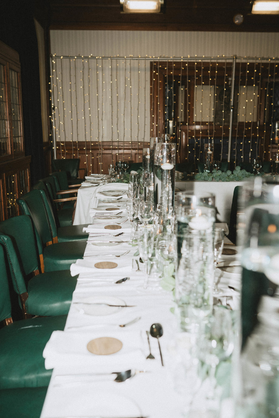 Long table set for wedding meal with green chairs and fairy lights