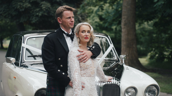 Bride and groom pose in front of wedding car