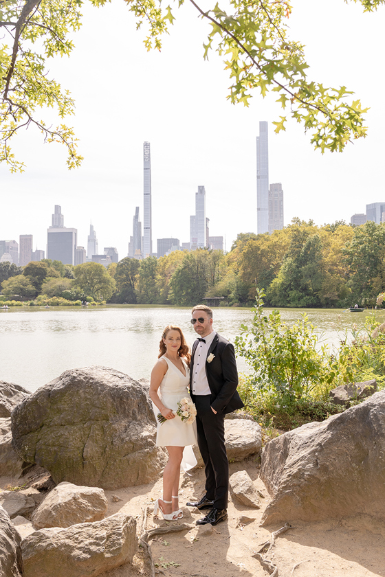Bride and groom posing beside a lake in Central Park with New York City skyline in the background