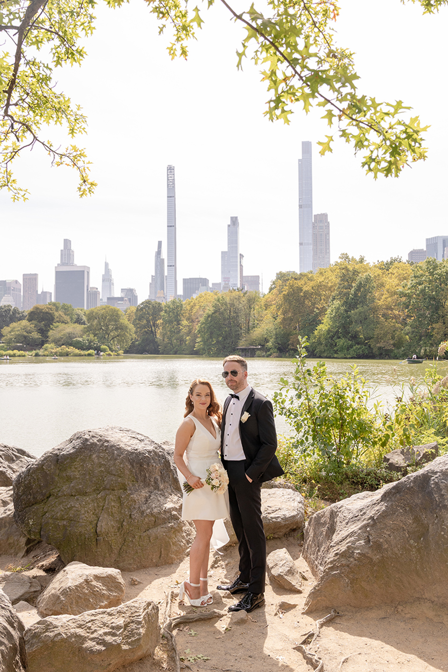 Bride and groom posing beside a lake in Central Park with New York City skyline in the background