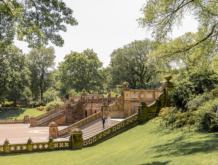 Wedding couple walking down ornate stone steps in Central Park, New York, surrounded by trees
