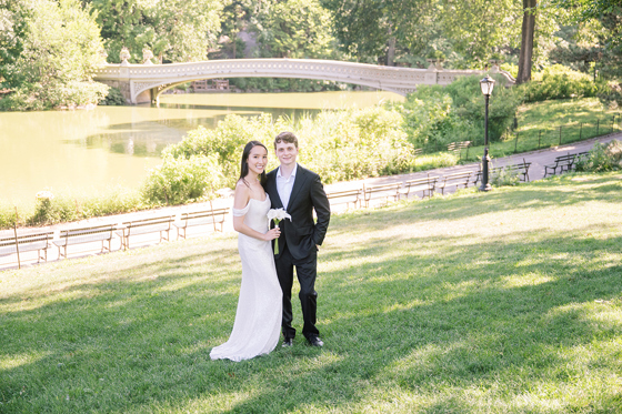 Wedding couple posing on the lawn in Central Park with Bow Bridge visible in the background