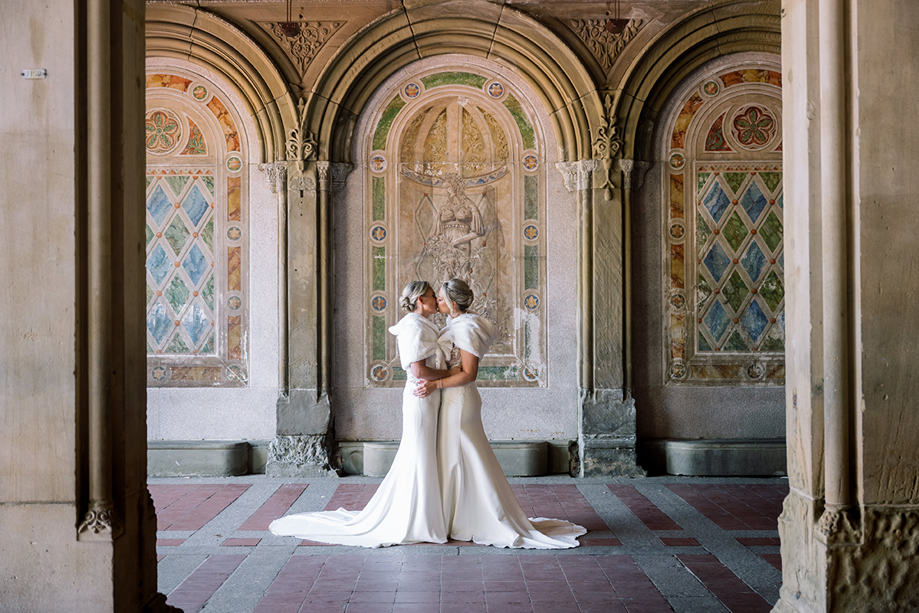 Two brides sharing a kiss in an ornate historic arcade in Central Park, New York wedding