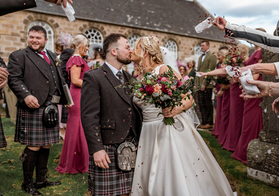 Bride and groom share a kiss during confetti shot by Magic Moments Studio