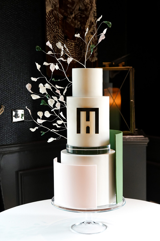 Three-tier white, baby pink, green and black cake with strands of leaves and design on front by YiShi Cake