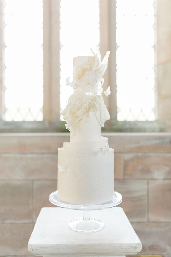 White three-tier cake on transparent stand with signature ruffles and butterfly detailing by YiShi Cake