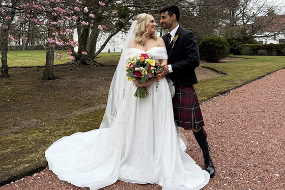 Bride and groom look at each other outside following their ceremony. Bride is holding a vibrant bouquet and groom is wearing a matching buttonhole. Image captured by Scottish wedding content creator Unveiled Moments.