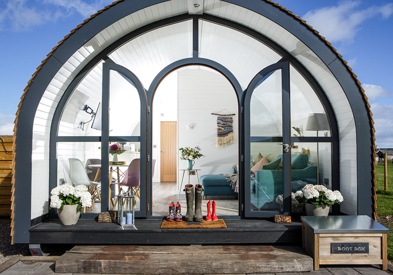 Glamping pod at Maycroft Retreat with bright, modern interiors with three pairs of welly boots outside door.