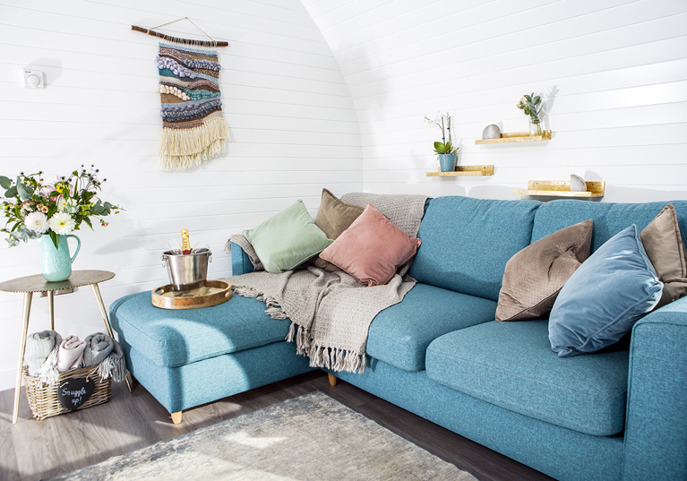 Inside a Maycroft Retreat glamping pod, featuring a bright blue L-shaped couch and ice bucket with champagne.