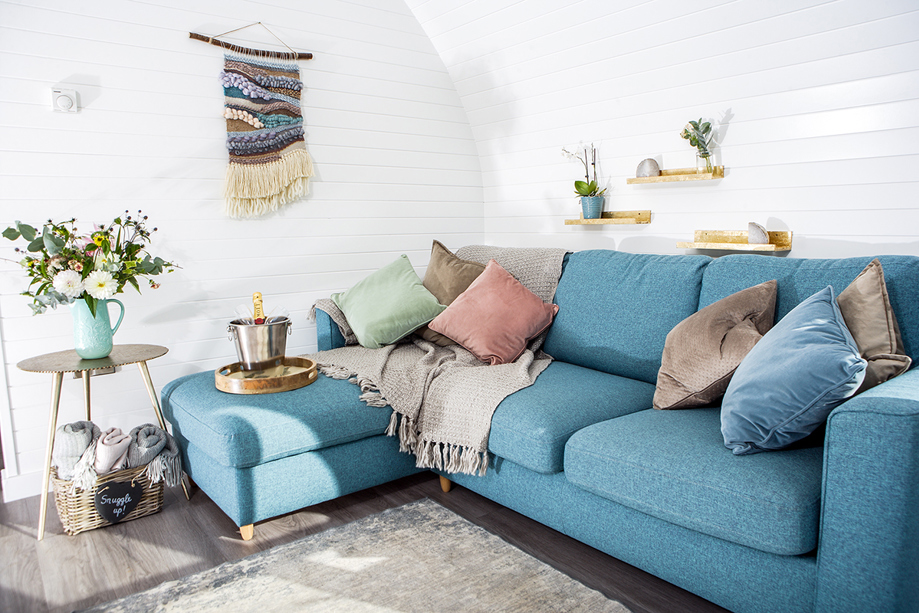 Inside a Maycroft Retreat glamping pod, featuring a bright blue L-shaped couch and ice bucket with champagne.