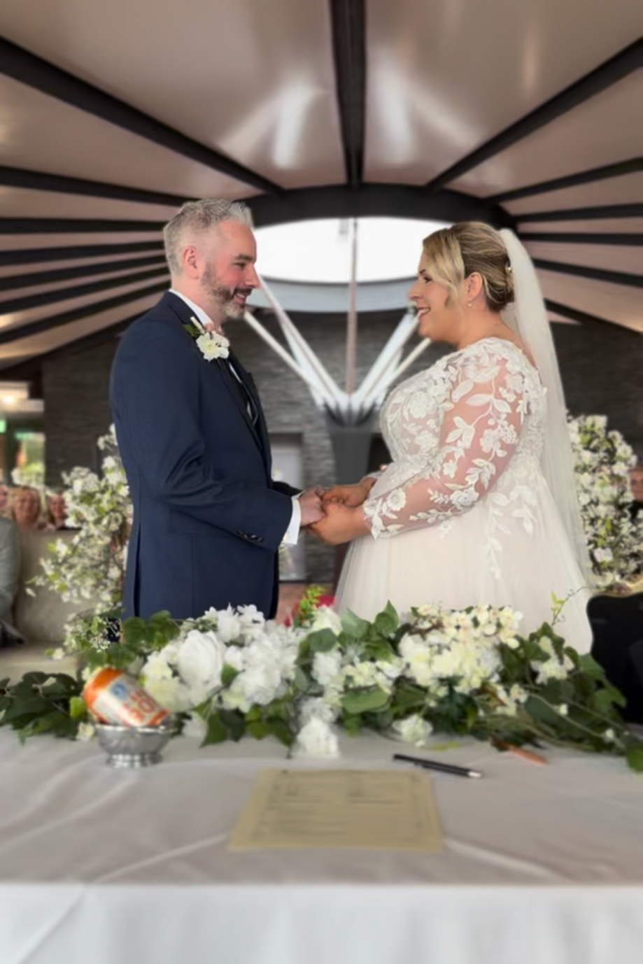 Bride and groom hold each others hands in front of registry table.