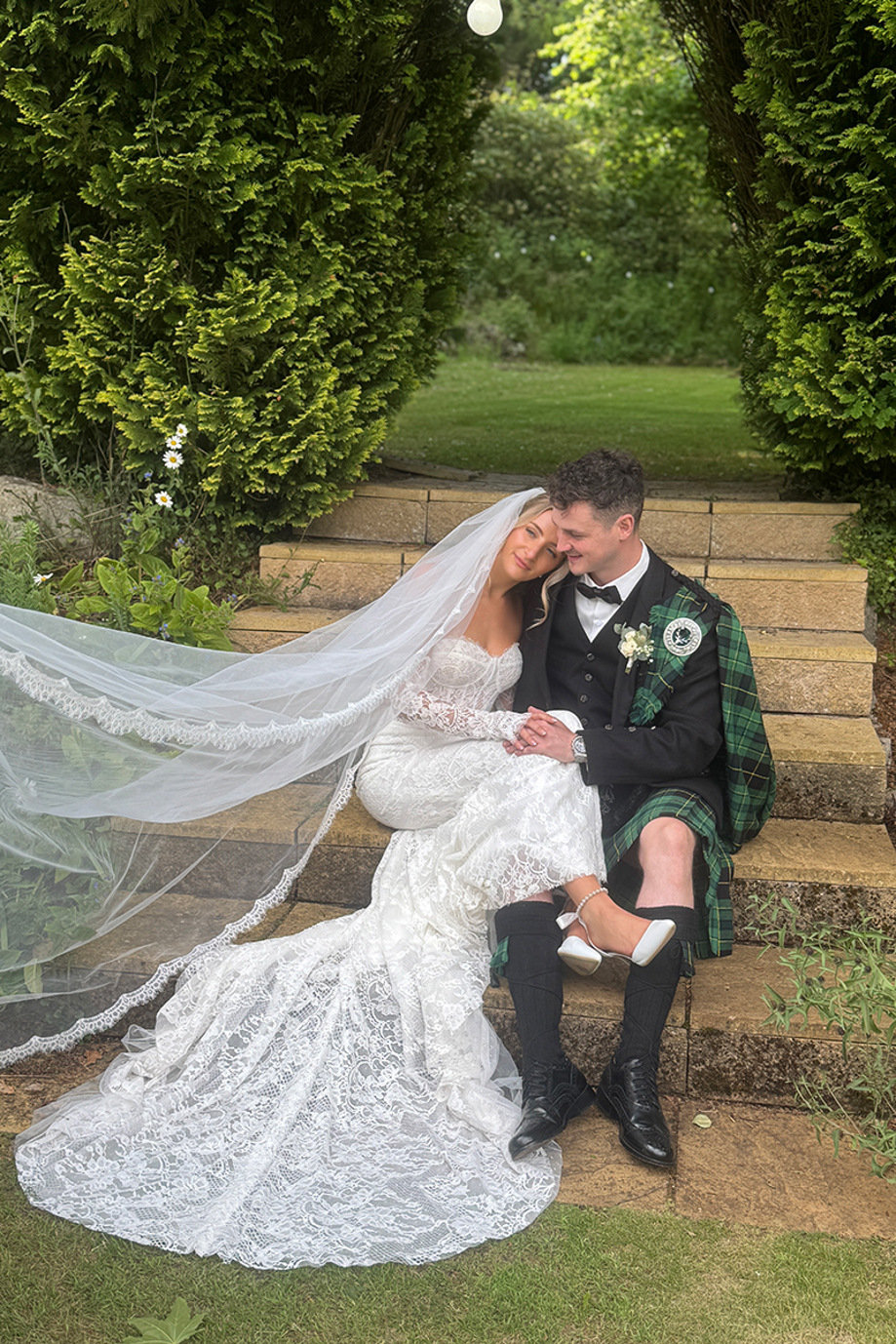Bride rests her head on grooms shoulder while sitting on steps in gardens of wedding venue, captured by Scottish wedding content creator The Perfect Day Club.
