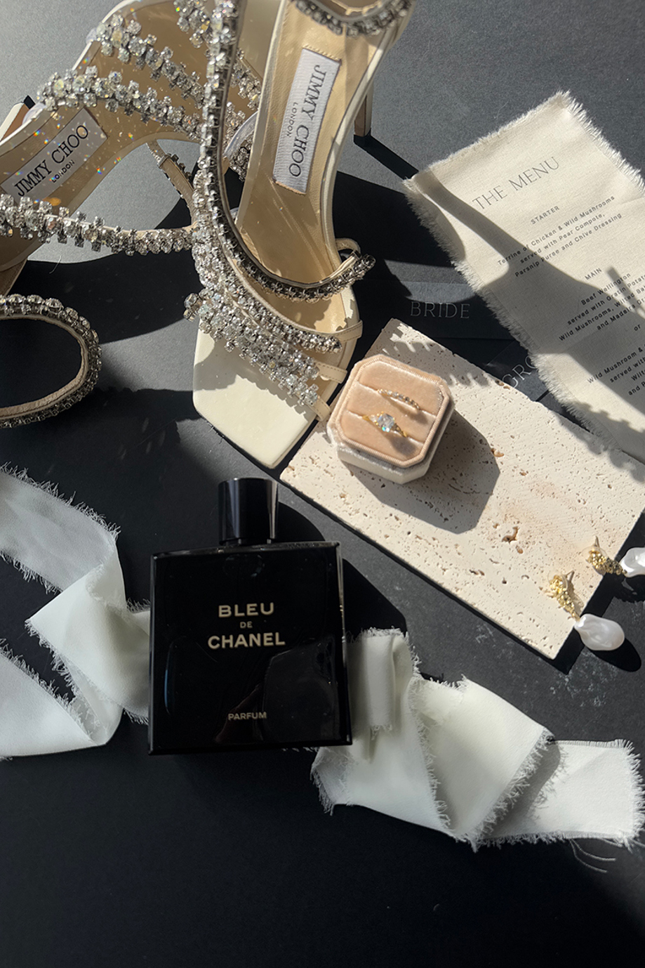 Detail shot of Jimmy Choo wedding shoes, rings, perfume and menu by The Perfect Day Club, a wedding content creator in Scotland.