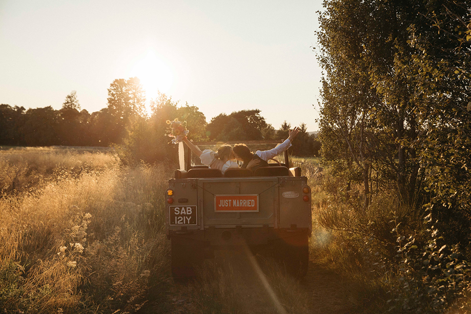 Bride and groom kiss as they drive away in green Range Rover at sunset. Wedding planning by Scottish Highlands-based wedding planners, Speyside Events Company.