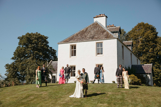 Bride and groom pose outside wedding venue with wedding party posing in twos behind them.