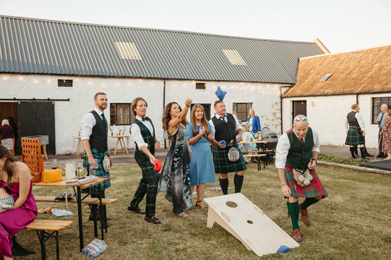 Guests play bean bag toss game outside wedding venue, organised by Scottish wedding planners Speyside Events Company.