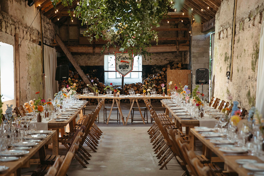 Organised by Speyside Events Company, long tables set up for wedding meal in barn setting and greenery hanging from ceiling.