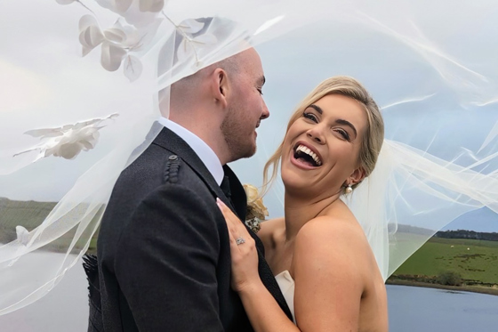 Bride laughs as her and her groom pose beneath veil by Millar Moments.