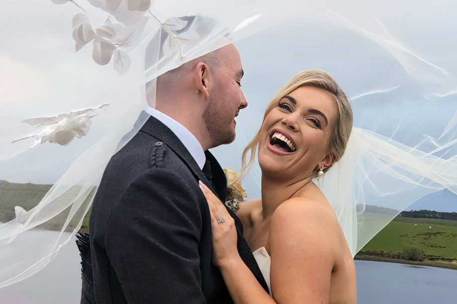 Bride laughs as her and her groom pose beneath veil by Millar Moments.