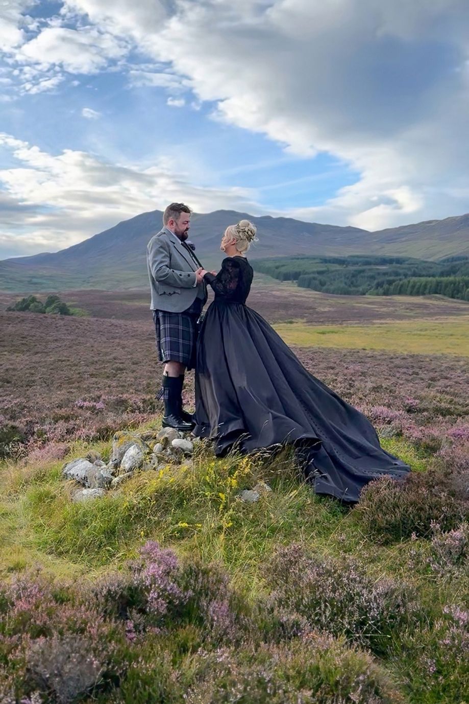 Bride in black wedding dress poses with her groom with Scottish hills in background, captured by Millar Moments.