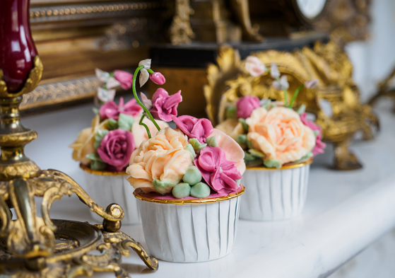 Hand-piped floral cupcakes in gold-rimmed white cupcake holders by Eclectic Luxuries