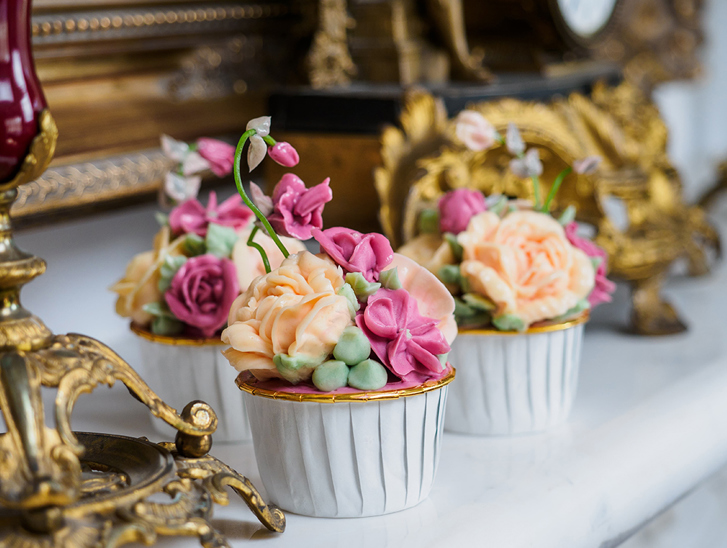 Hand-piped floral cupcakes in gold-rimmed white cupcake holders by Eclectic Luxuries
