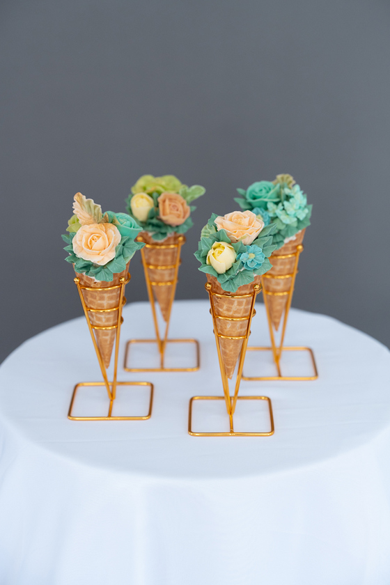 Four hand-piped cones in gold stands on a round table with a white tablecloth by Eclectic Luxuries - Artisan Couture Cakes