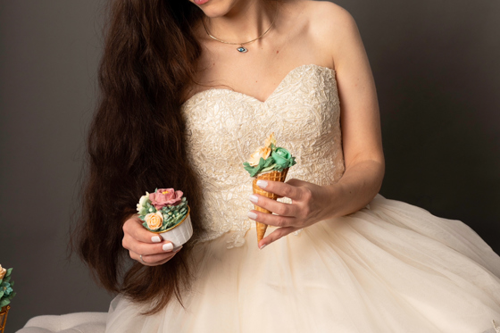 Cake designer at Eclectic Luxuries in a pink dress holds a hand-piped floral cone and hand-piped floral cupcake.