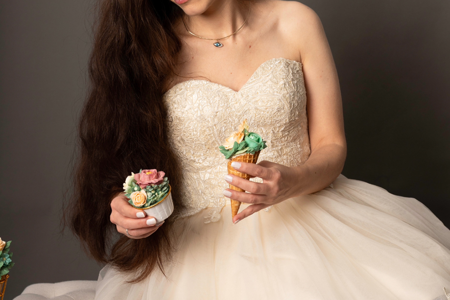 Cake designer at Eclectic Luxuries in a pink dress holds a hand-piped floral cone and hand-piped floral cupcake.