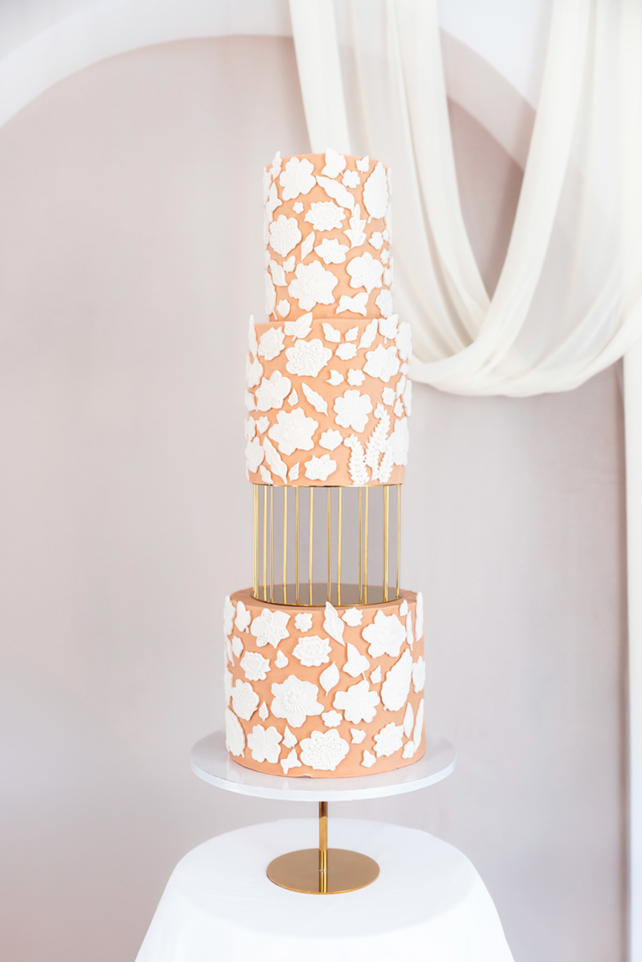 Peach and white four-tier cake with white fondant flowers and a third gold cake spacer tier