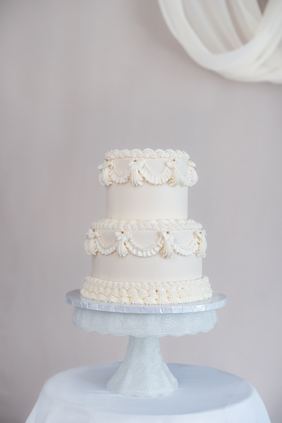 White Lambeth-style piped two-tier cake on a stand against a white background by Eclectic Luxuries