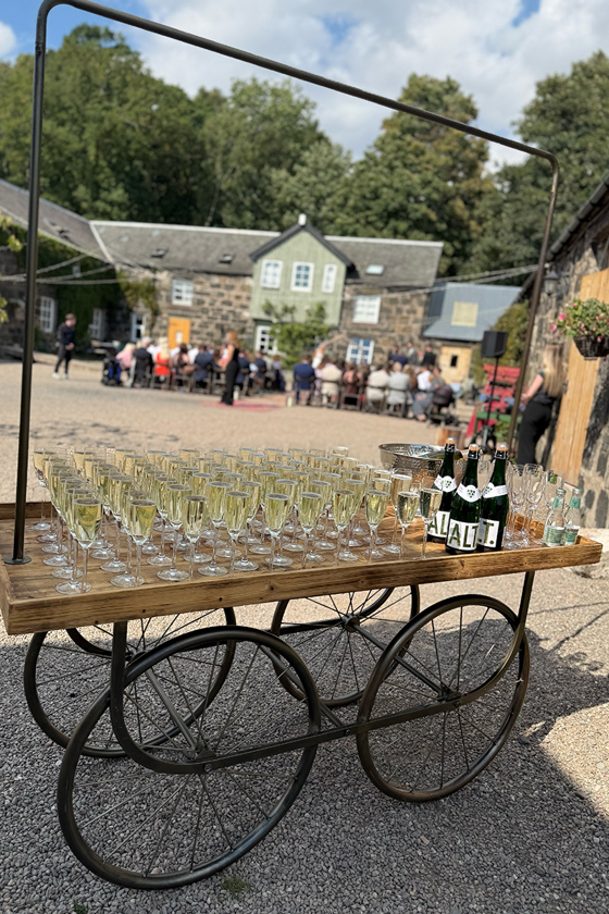 Cart with glasses of Champagne and bottles in courtyard of Scottish wedding venue.