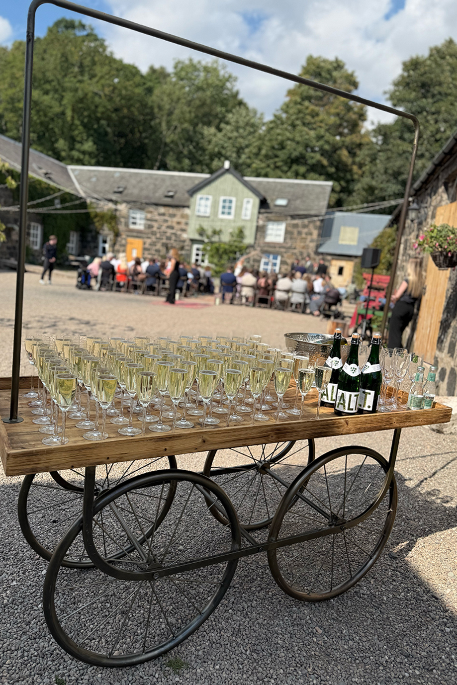 Cart with glasses of Champagne and bottles in courtyard of Scottish wedding venue.