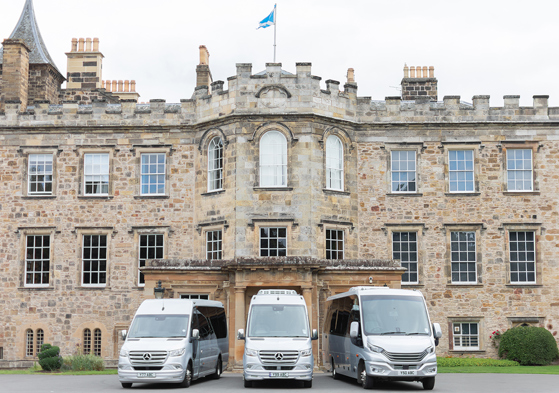 Three buses from Anderson Black Executive Travel's fleet parked outside the doors of Scottish castle wedding venue with Saltire flying overhead
