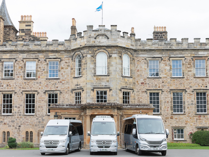 Three buses from Anderson Black Executive Travel's fleet parked outside the doors of Scottish castle wedding venue with Saltire flying overhead