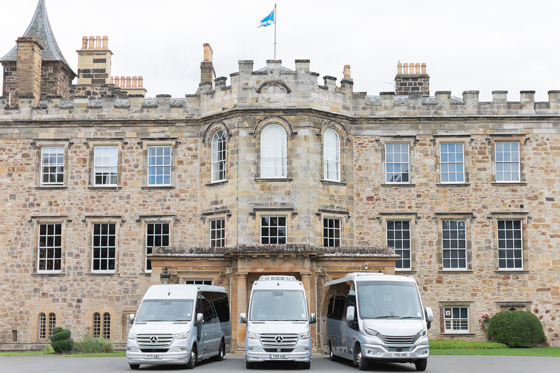 Three buses from Anderson Black Executive Travel's fleet parked outside the doors of Scottish castle wedding venue with Saltire flying overhead