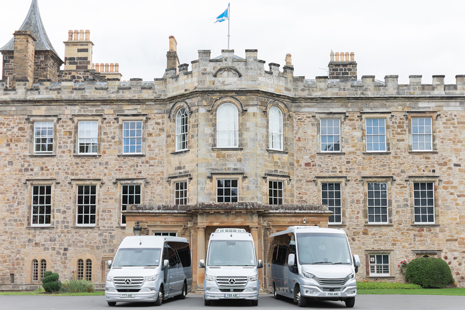 Three buses from Anderson Black Executive Travel's fleet parked outside the doors of Scottish castle wedding venue with Saltire flying overhead
