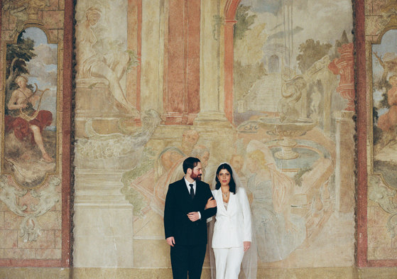 groom and bride in white suit standing in front of painted wall